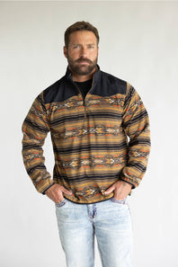 A close-up of a person wearing a quarter-zip fleece pullover with a black collar and a Southwestern geometric pattern in beige, brown, yellow, and orange. The brand name 'ARIAT' is visible on a small patch on the chest.