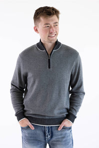 A smiling male model wearing the F/X Fusion Birdseye Knit Quarter Zip in nickel gray, featuring a mock neck, quarter-zip placket, and dark contrasting trim along the collar, cuffs, and hem, paired with classic denim jeans.