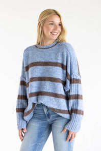 A woman wearing a light blue and brown striped knit sweater with light wash blue jeans, standing against a plain white background.