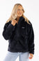 A woman wearing a black fleece zip-up jacket and light blue jeans, photographed against a plain white studio background.