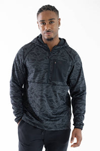 A man wearing a dark gray and black camouflage patterned quarter-zip hoodie with a chest pocket, photographed against a solid white background.