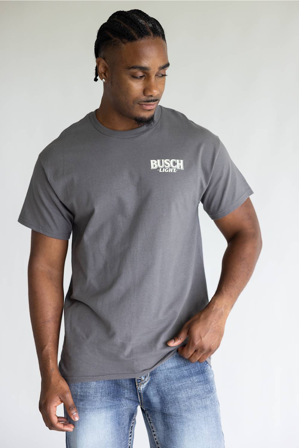A man wearing a dark gray crewneck t-shirt with a white 'BUSCH LIGHT' logo on the left chest, paired with blue jeans, photographed against a light gray studio background.