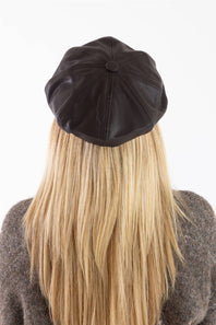 A view from behind of a person with long blonde hair wearing a dark chocolate brown faux leather newsboy hat with a stitched panel design, seen against a plain white background.