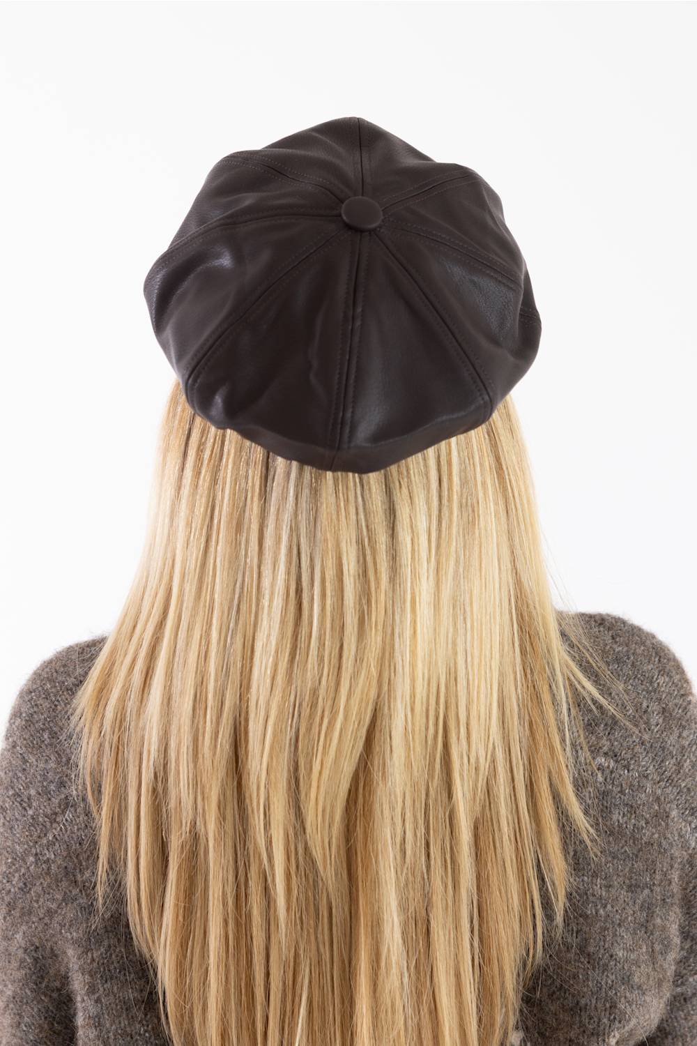 A view from behind of a person with long blonde hair wearing a dark chocolate brown faux leather newsboy hat with a stitched panel design, seen against a plain white background.