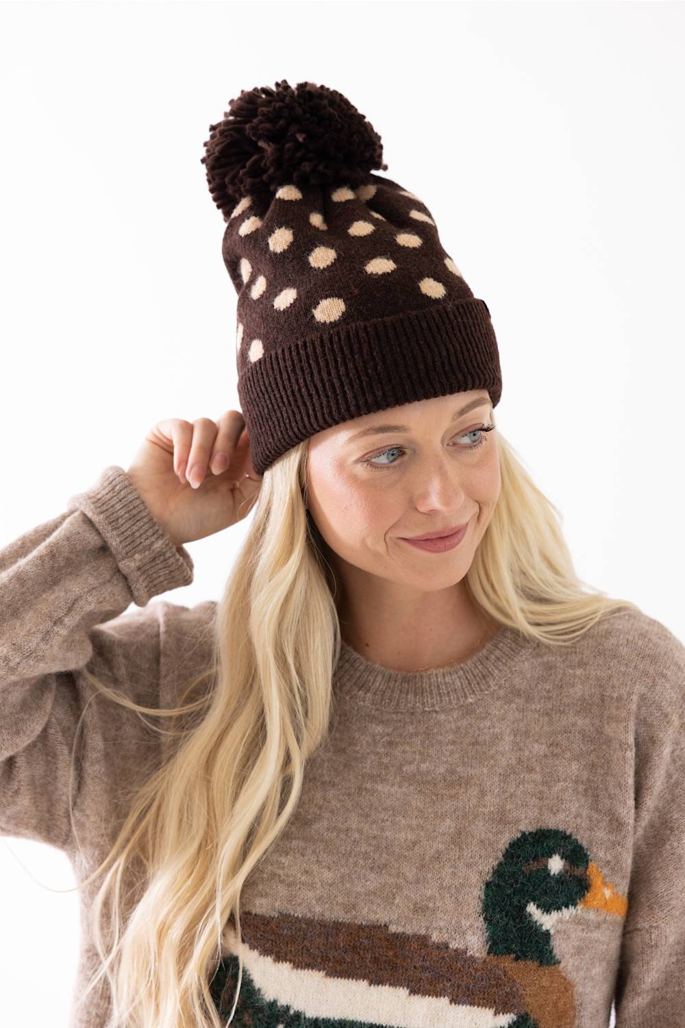 C.C. Polka Dot Pom Beanie for Women in Brown. A close-up view of the back of the knit hat, showing the brown main color, cream polka dots, dark brown fuzzy pom-pom, and ribbed cuffed hem.