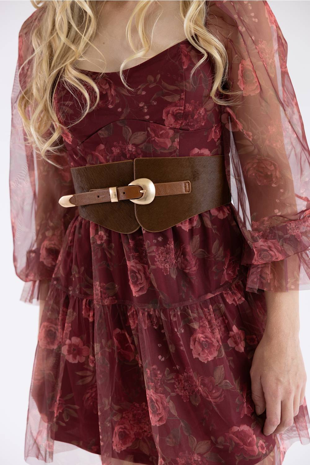A close-up of a model wearing a dark red floral dress with a wide brown leather belt featuring a gold buckle.