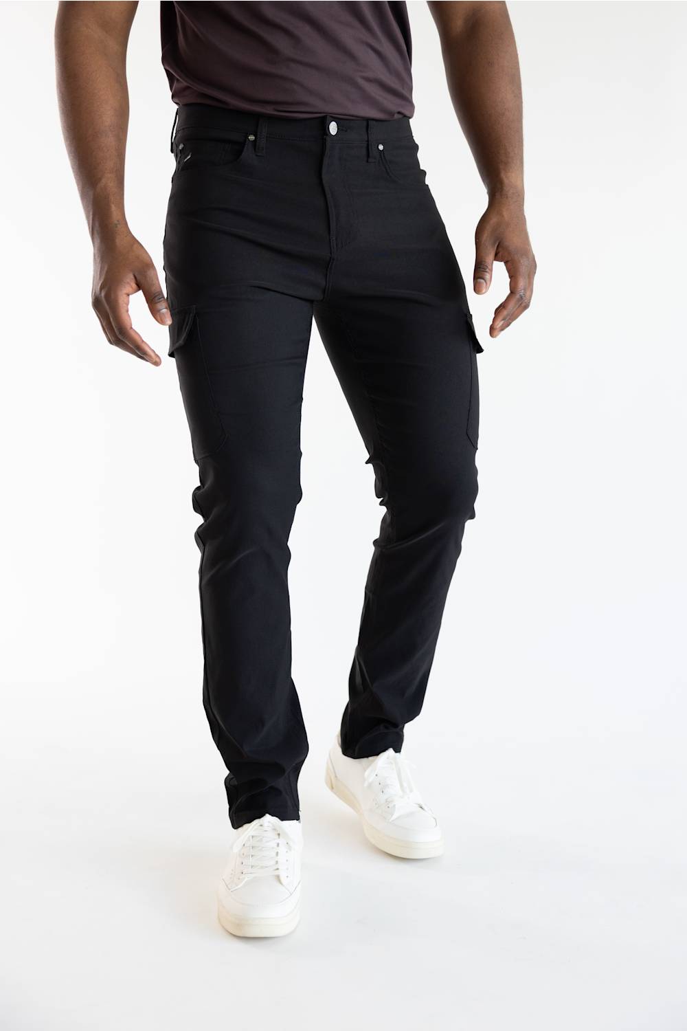 A model wearing black cargo-style slim-fit jeans with white sneakers, shown from the waist down against a plain white studio background.
