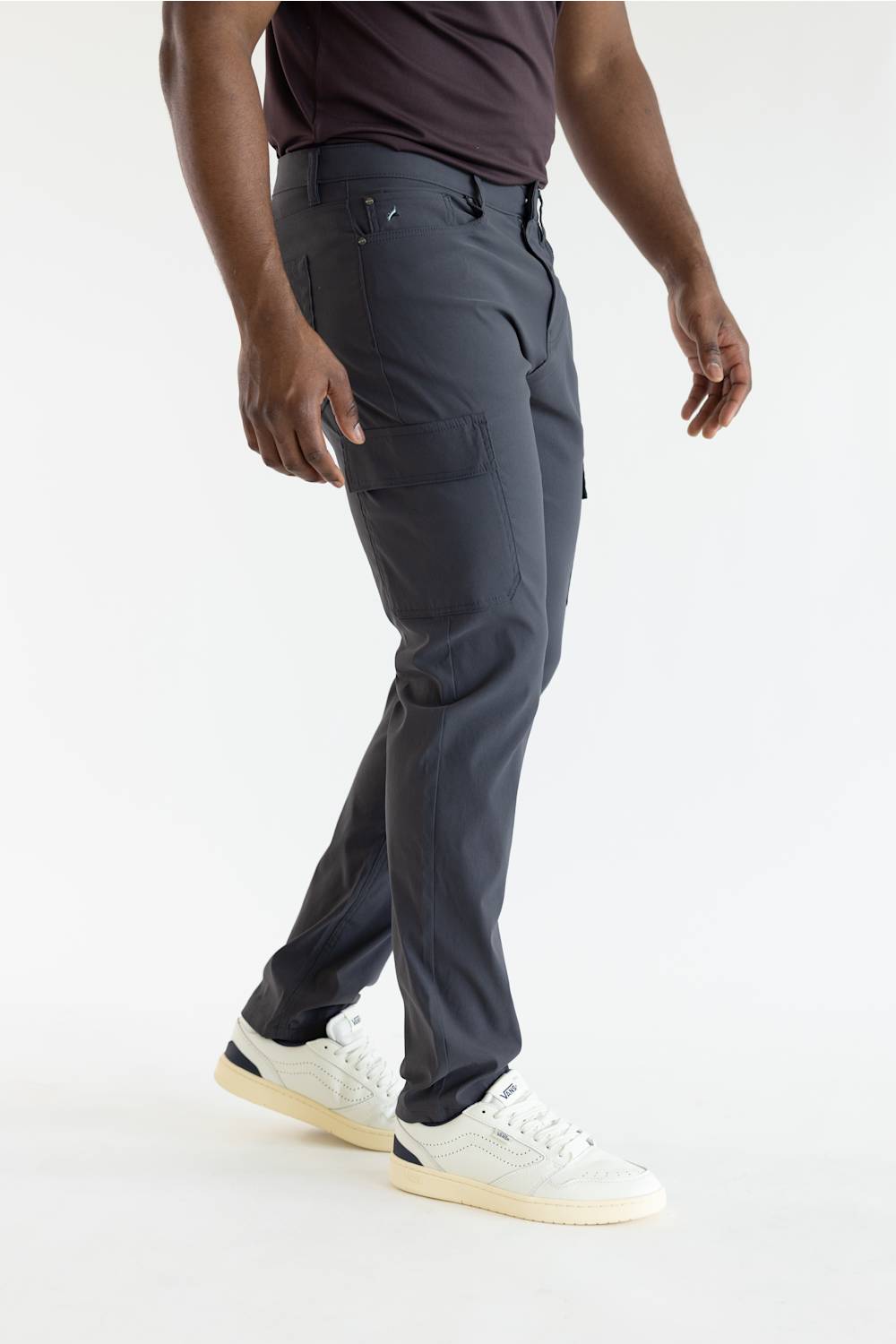 A person wearing dark charcoal gray cargo pants, a dark t-shirt, and white sneakers, shown from the waist down against a plain white studio background.