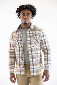 A man wearing a beige, brown, and gray plaid button-up flannel shirt over a gray t-shirt and khaki pants, standing against a plain white background.