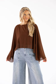 A woman modeling a brown long-sleeve top with wide draped bell sleeves, paired with light blue wide-leg jeans and a patterned headband, against a plain white background.