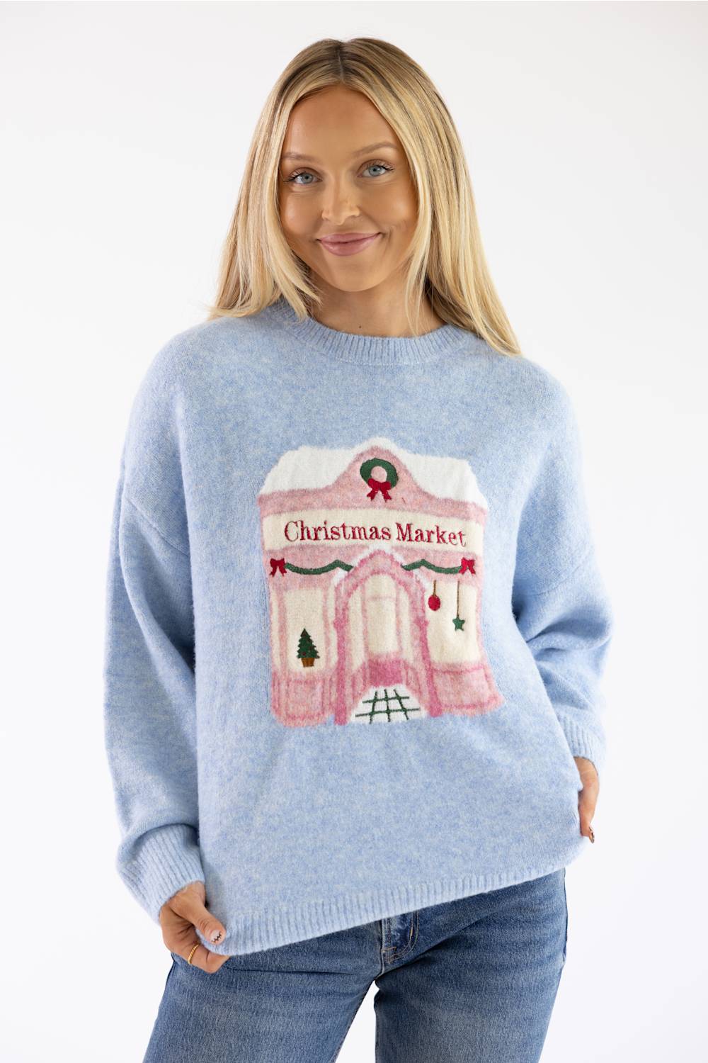 Blonde woman modeling a periwinkle blue christmas market storefront sweater with jeans
