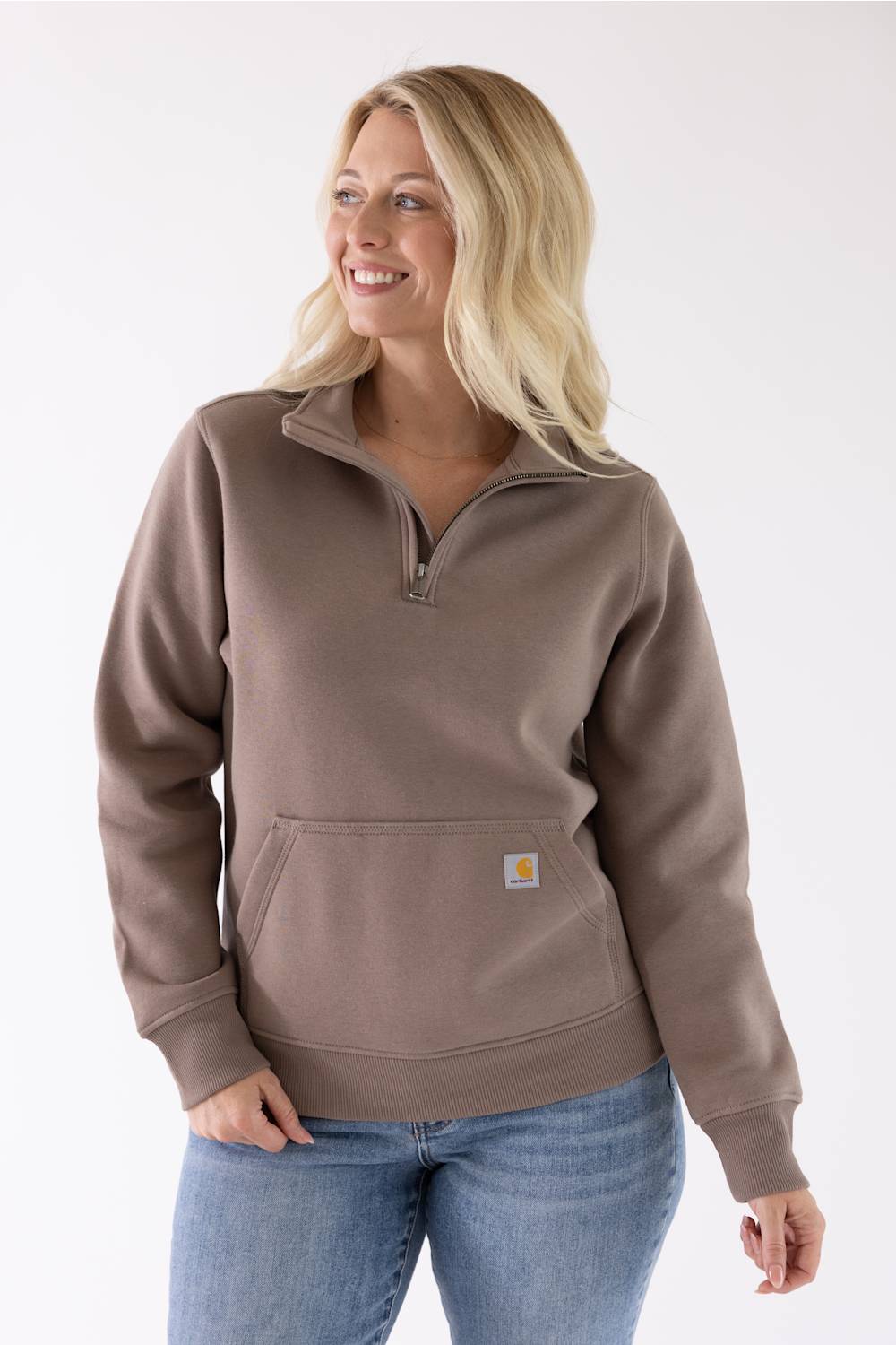Front view of a stone brown Carhartt quarter-zip sweatshirt featuring a mock-neck collar and a front kangaroo pocket with a small logo patch, worn with blue jeans.