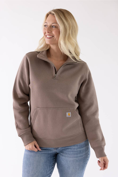 Front view of a stone brown Carhartt quarter-zip sweatshirt featuring a mock-neck collar and a front kangaroo pocket with a small logo patch, worn with blue jeans.