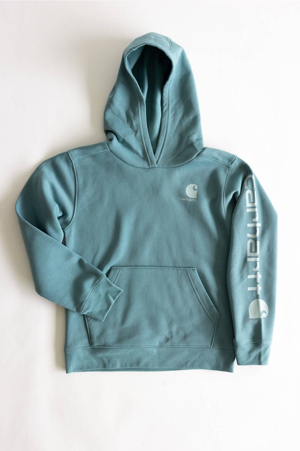A teal blue-green Carhartt pullover hoodie laid flat on a light off-white background. The hoodie features a small white Carhartt logo on the left chest and a large white vertical Carhartt logo printed down the right sleeve.