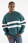 A man wearing a teal green hooded sweatshirt with white and navy blue stripes on the sleeves, paired with light-wash blue jeans, against a plain white background.