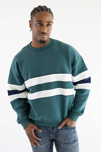 A man wearing a teal green hooded sweatshirt with white and navy blue stripes on the sleeves, paired with light-wash blue jeans, against a plain white background.