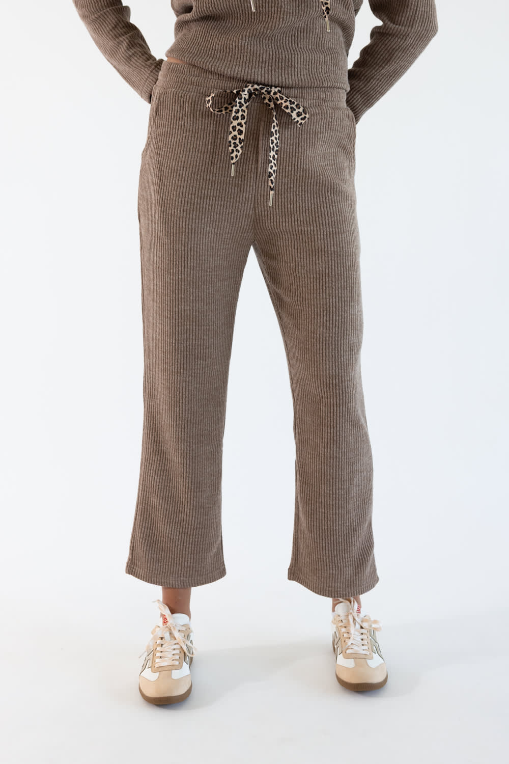 A person wearing corduroy lounge pants in sand-brown with a leopard-print drawstring, paired with a matching top and beige sneakers, shown against a plain light background.
