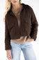 A woman wearing a dark brown cropped utility jacket over a beige ribbed sweater and light blue jeans, shown from the waist up against a plain white background.
