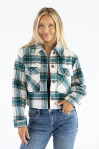 A woman modeling a cropped long-sleeve plaid flannel jacket in green, white, and gray, paired with blue jeans against a plain white background.