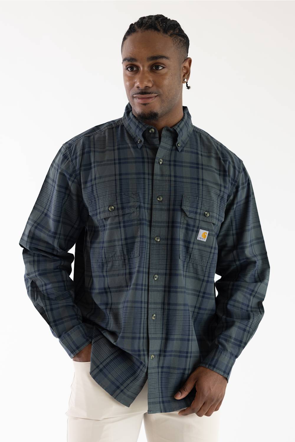 Male model in a loose-fit Carhartt navy and green long-sleeve plaid shirt featuring two button-flap chest pockets and a Carhartt logo patch on the left chest.
