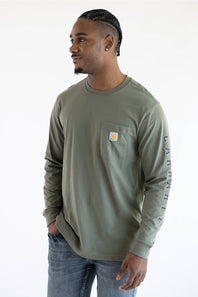 A man wearing the Carhartt Irvine Relaxed Pointer Dog Long Sleeve T-Shirt for Men in Dusty Olive Green featuring a Carhartt logo down the left arm and a classic Carhartt patch logo with front pocket located on the upper left chest.