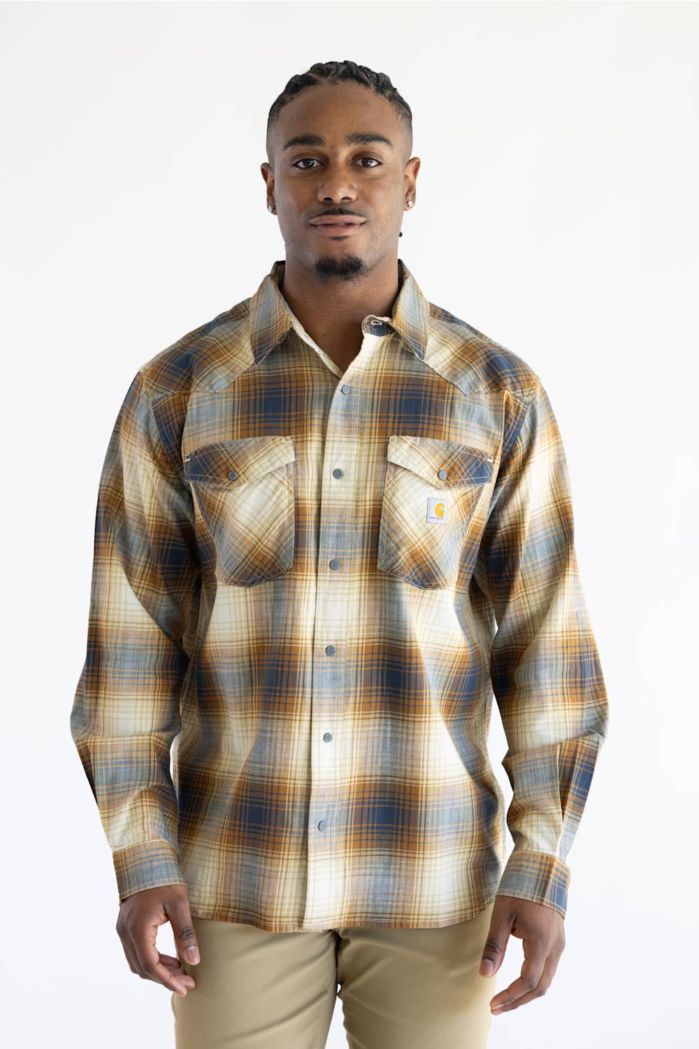 A man wearing a Carhartt long-sleeve plaid button-up shirt in beige, brown, and blue tones, paired with khaki pants, against a plain white background.