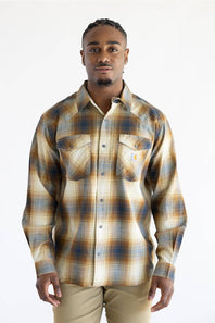 A man wearing a Carhartt long-sleeve plaid button-up shirt in beige, brown, and blue tones, paired with khaki pants, against a plain white background.