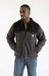 A man in a brown jacket and blue jeans stands against a plain white background.