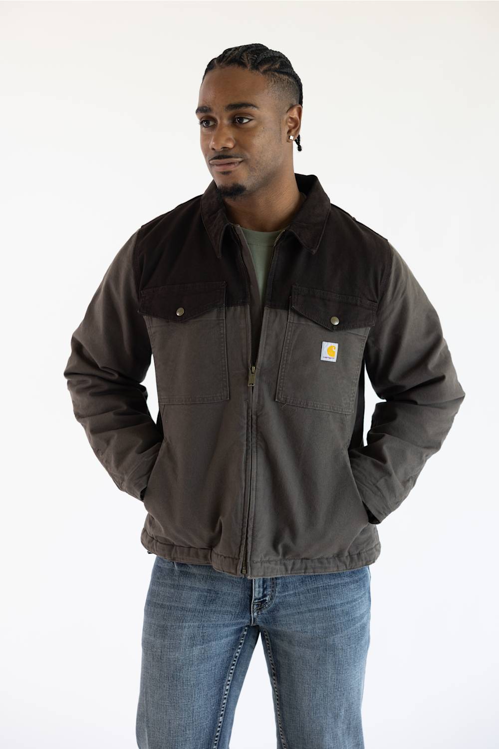 A man in a brown jacket and blue jeans stands against a plain white background.