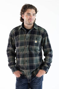 A man wearing a Carhartt long-sleeve plaid button-up shirt in dark green, black, and gray, paired with blue jeans, against a plain white background.