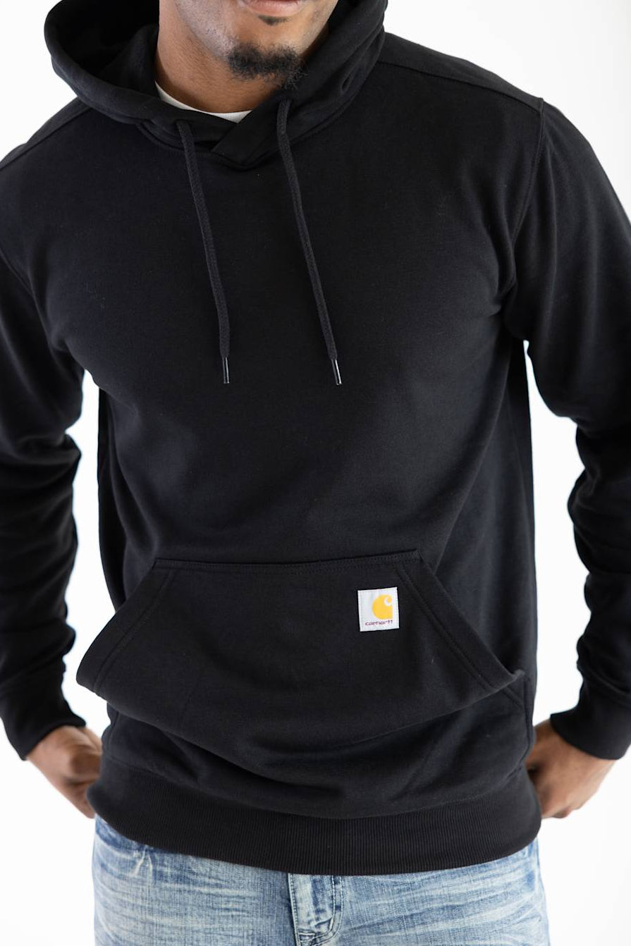 Close-up, cropped view of a male model wearing the black Carhartt Sawyer deer hoodie, showing the drawstring hood, front kangaroo pocket, and small Carhartt logo patch.