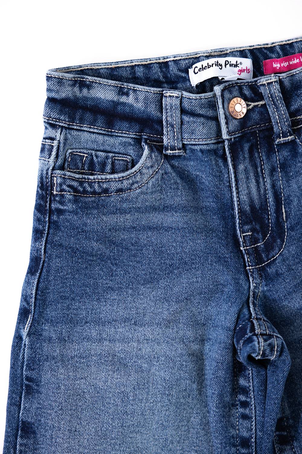 Close-up front view of Celebrity Pink youth girls' medium wash denim jeans highlighting the waistband, button closure, coin pocket, and white inner tag reading "Celebrity Pink girls".