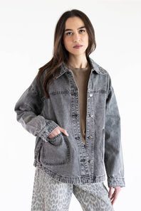 A woman modeling an oversized, washed gray denim jacket over a brown top and leopard-print pants against a plain white background.