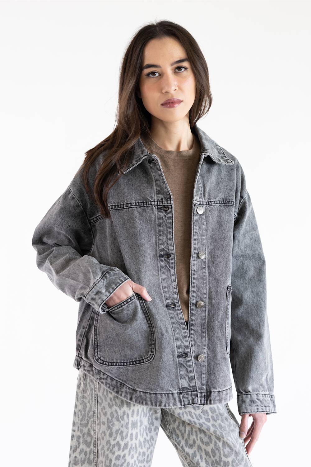 A woman modeling an oversized, washed gray denim jacket over a brown top and leopard-print pants against a plain white background.