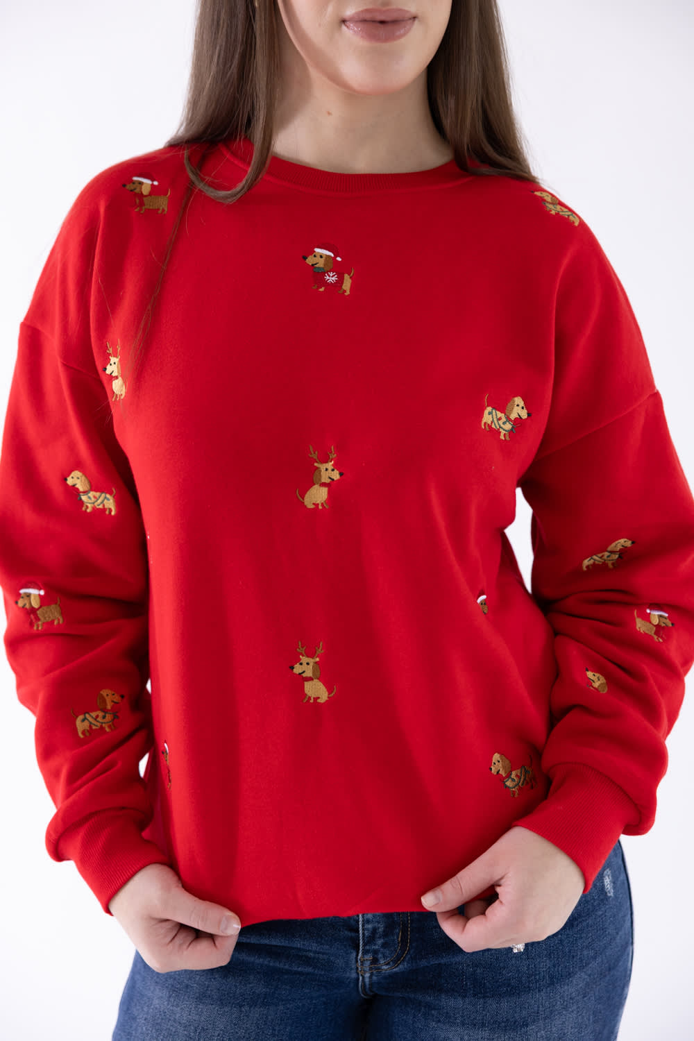 A woman wearing a bright red crewneck sweatshirt with small embroidered golden deer motifs, paired with blue jeans against a plain white background.