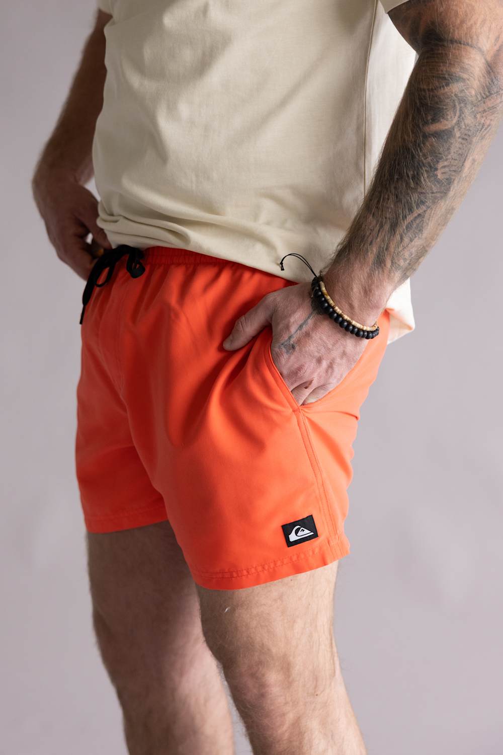 Person wearing orange shorts with a visible brand logo on a plain background. The shorts are Quiksilver Everyday Solid Volley 15" Swim Shorts for Men in Hot Coral