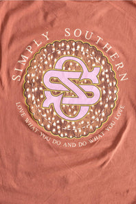 A close-up of a peach-pink fabric surface featuring a large circular graphic with the words 'SIMPLY SOUTHERN' and a pink monogram logo in the center.