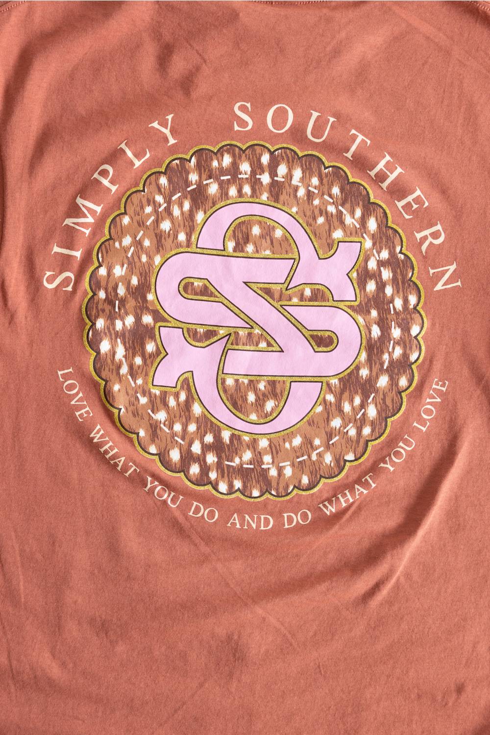 A close-up of a peach-pink fabric surface featuring a large circular graphic with the words 'SIMPLY SOUTHERN' and a pink monogram logo in the center.