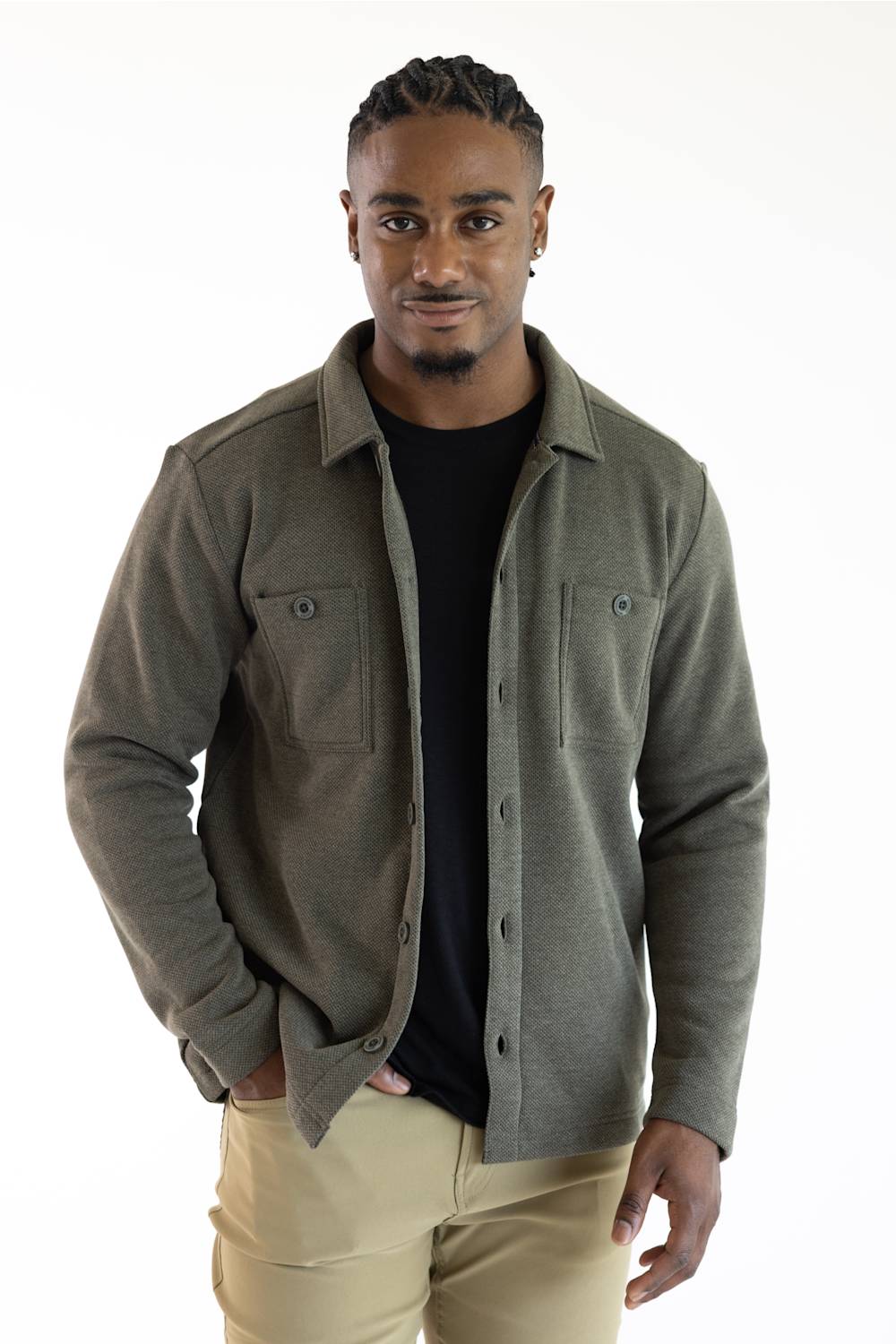 A man wearing a dark olive green button-up overshirt over a black t-shirt and khaki pants, standing against a plain white background.