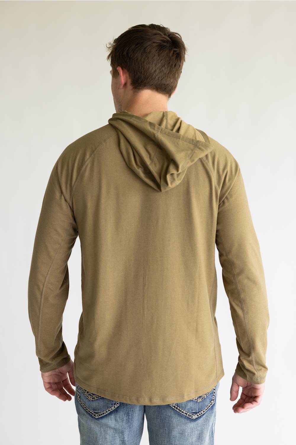 A man viewed from behind wearing a tan long-sleeve hooded shirt and blue jeans against a plain light background.