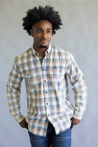 A man wearing a long-sleeve plaid button-down shirt with blue, beige, and white tones, paired with blue jeans, standing against a neutral gray background.