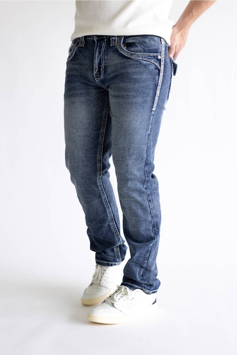 A person wearing blue denim jeans with white sneakers, shown from the waist down against a plain light background.