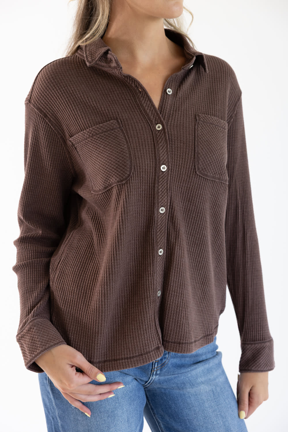 A woman wearing a brown ribbed long-sleeve button-up shirt with chest pockets, paired with blue jeans, shown against a plain white background.