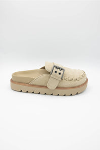 A single beige slip-on clog-style shoe with a braided strap detail and a silver-tone buckle, shown on a light gray background.