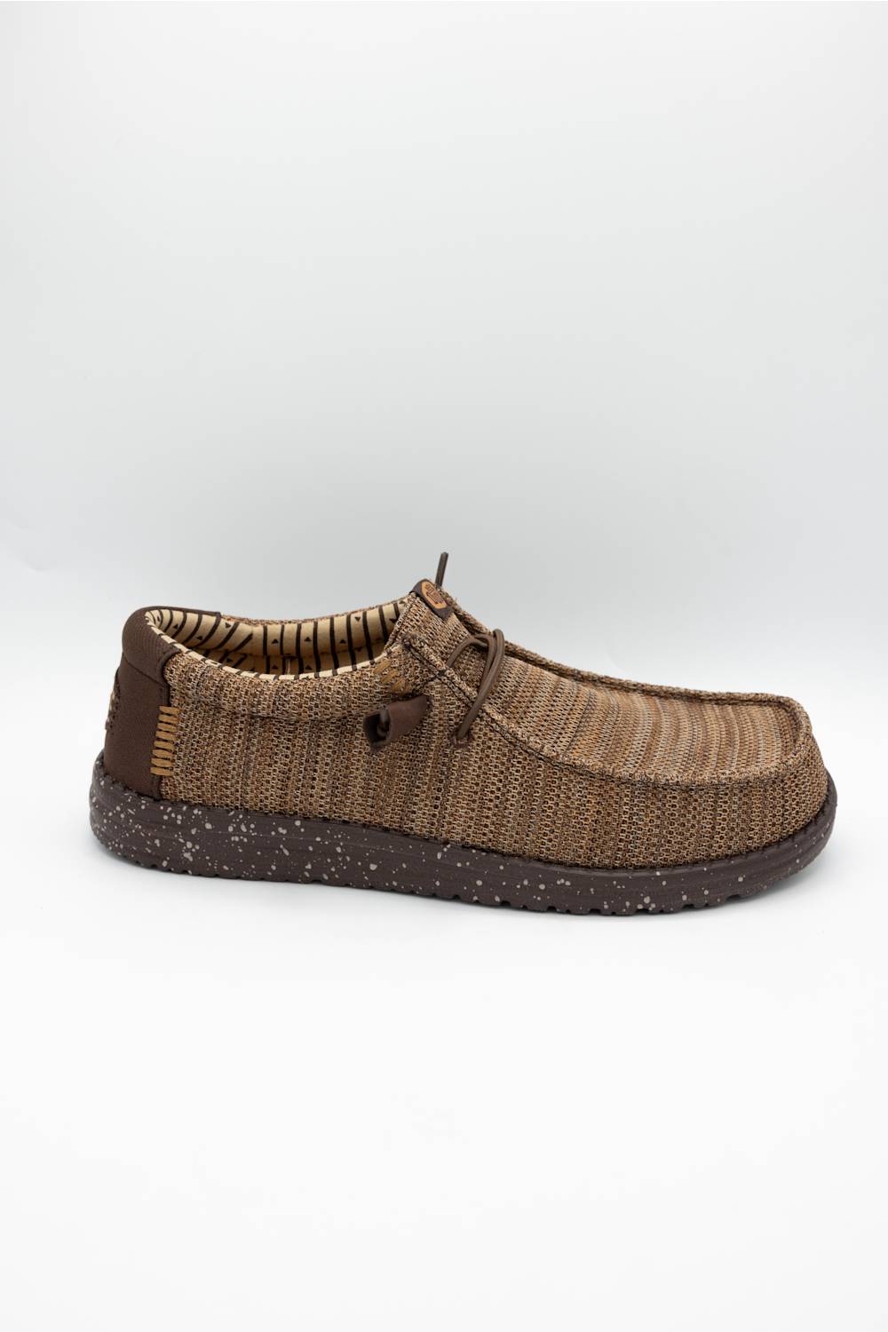 A single brown woven slip-on shoe with a textured knit upper, matching laces, and a speckled dark brown sole, shown against a plain light gray background.