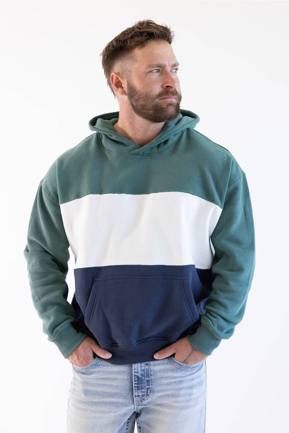 A man wearing a color-block hoodie with green, white, and navy blue sections, paired with light-wash jeans, photographed against a plain white background.