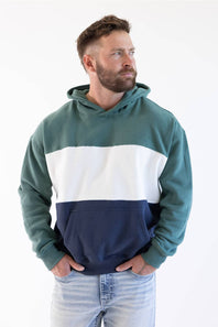 A man wearing a color-block hoodie with green, white, and navy blue sections, paired with light-wash jeans, photographed against a plain white background.