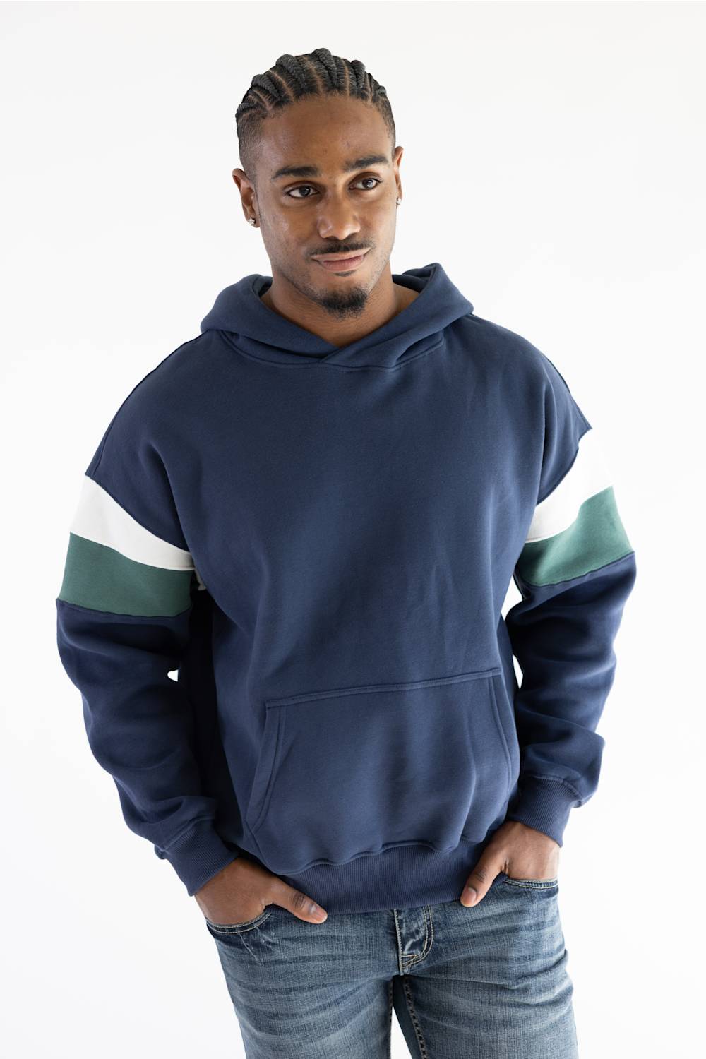 A man wearing a navy blue hoodie with green and white color-blocked sleeves, paired with blue jeans, standing against a plain white background.