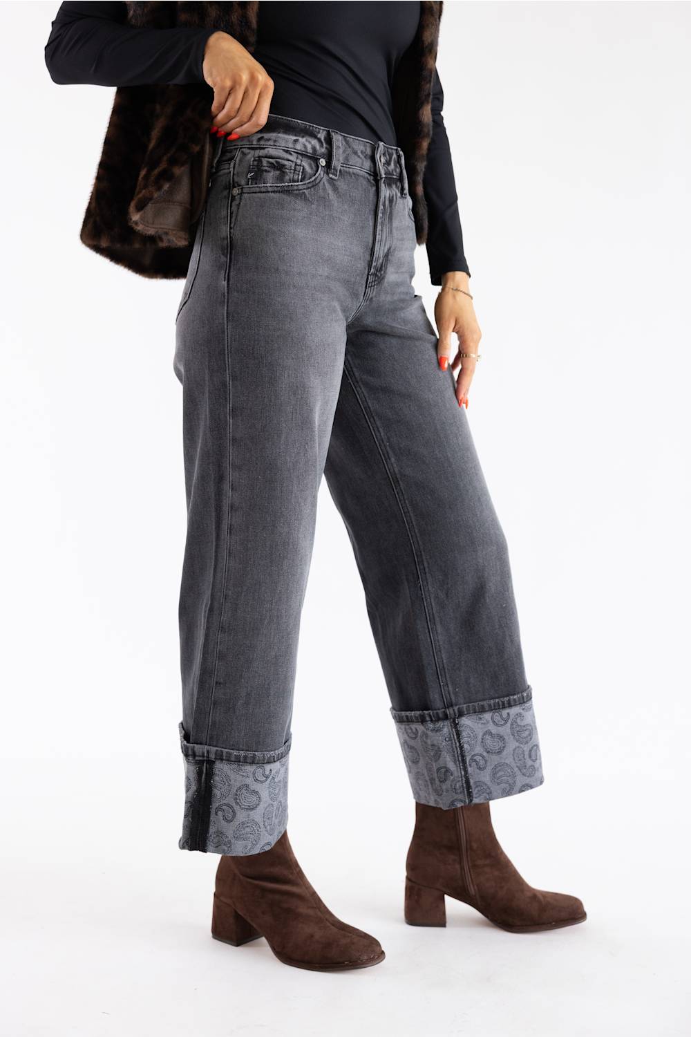 A model wearing a pair of dark gray washed wide-leg jeans with rolled cuffs showing a patterned lining, styled with brown suede ankle boots and a black top against a white studio background.