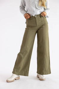 A model wearing olive green wide-leg pants, styled with a light gray cable-knit sweater and white platform boots, standing against a plain white studio background.